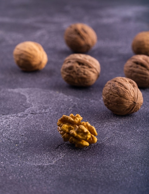 Całe i popękane orzechy włoskie na niebieskiej powierzchni teksturowanej, widok z boku. Zdrowy skład orzechów i nasion.