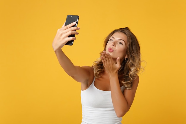 Całkiem młoda kobieta dziewczyna w lekkie ubrania dorywczo pozowanie na białym tle na żółtym pomarańczowym tle. Koncepcja życia ludzi. Makieta miejsca na kopię. Robienie selfie na telefonie komórkowym, wysyłanie pocałunku w powietrzu.