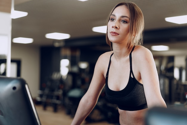 Całkiem sprawna kobieta w czarnym sportrswear szkolenia na bieżni w klubie fitness