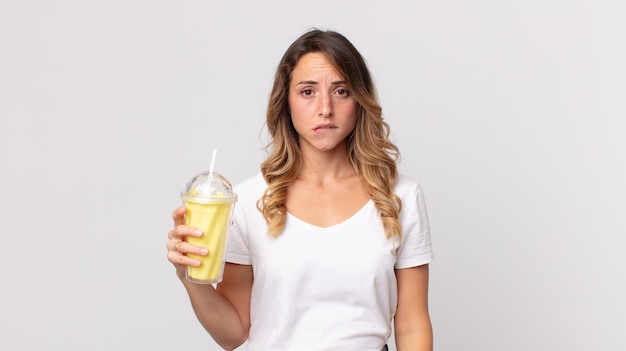 Całkiem szczupła kobieta wyglądająca na zdziwioną i zdezorientowaną, trzymająca waniliowego koktajlu mlecznego