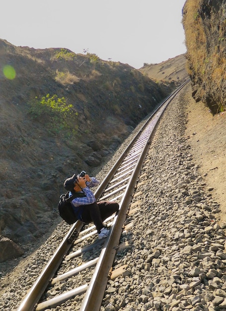 Zdjęcie całkowita długość mężczyzny fotografującego przez kamerę podczas przykucania się na torze kolejowym