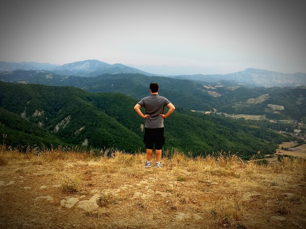 Zdjęcie całkowity widok z tyłu człowieka stojącego na wzgórzu przed górami na czyste niebo