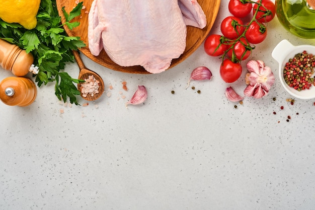 Cały surowy kurczak z dodatkami do przygotowania pieprzu, cytryny, tymianku, czosnku, pomidora koktajlowego, szczawiu i soli w kuchni na jasnoszarym tle łupkowym, kamiennym lub betonowym. Widok z góry z miejsca na kopię.