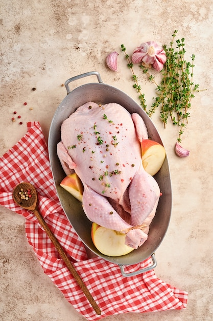 Cały surowy kurczak z dodatkami do przygotowania pieprzu, cytryny, tymianku, czosnku, pomidora, szczawiu, z jabłkami i solą w kuchni na ciemnym tle łupkowym, kamiennym lub betonowym. Widok z góry z miejsca na kopię.