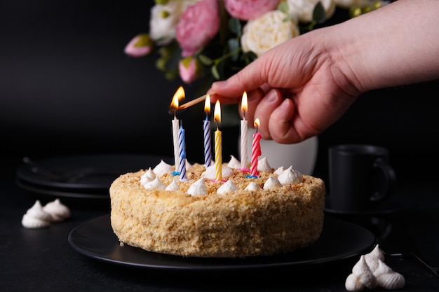 Zdjęcie cały tort świąteczny z kruchym ciastem i mini meringue mężczyzna zapala świece na torcie ciasto urodzinowe z zapalonymi świecami domowe pieczenie czarne tło selektywne skupienie zbliżenie