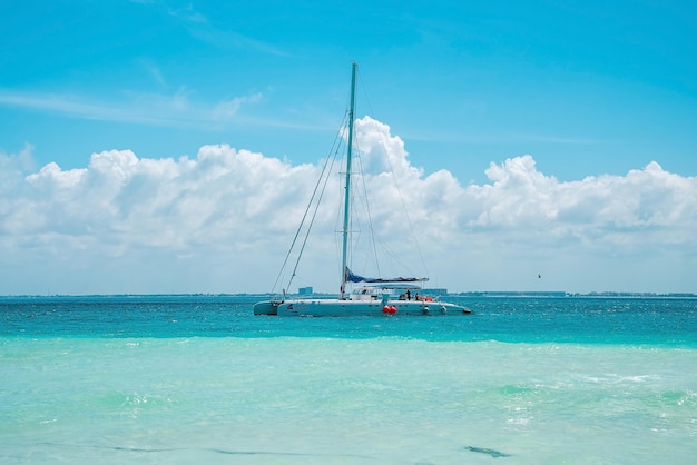 Cancún, Meksyk. 30 maja 2021 r. Jacht lub żaglówka płynąca po pięknej turkusowej powierzchni wody morskiej na tle zachmurzonego nieba