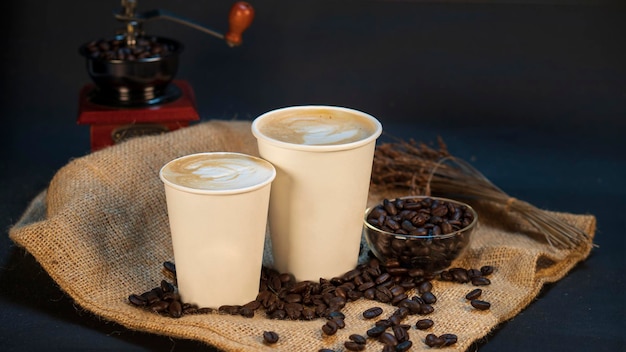 Cappuccino podane w papierowym kubku z ziarnami kawy posypanymi na wierzchu jutowego worka
