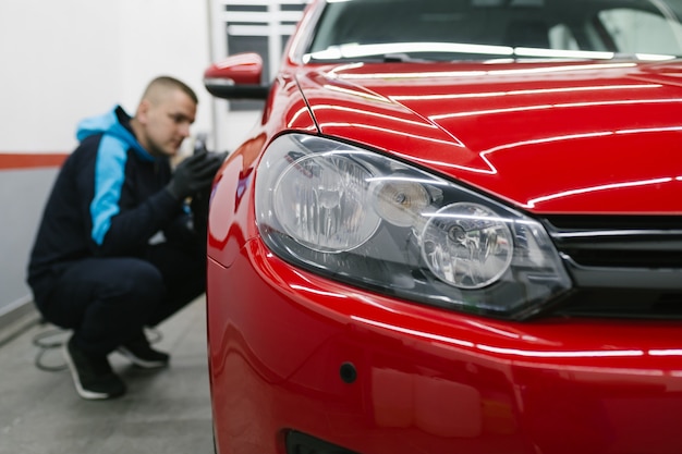 Car detailing - Człowiek z polerem orbitalnym w warsztacie polerującym samochód. Selektywne skupienie.