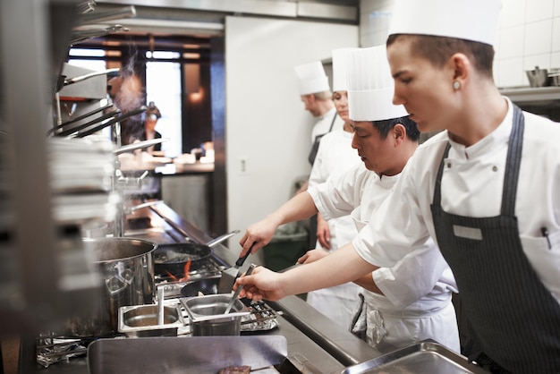 Catering profesjonalni szefowie kuchni gotujący jedzenie iw kuchni restauracji Obsługa lub wyśmienita gościnność lub zakwaterowanie i personel lub grupa osób przygotowujących posiłek na lunch lub kolację razem