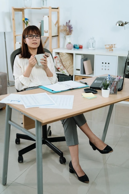 CEO kobiety patrzy w dal i zastanawia się nad swoją przyszłością w swoim biurze. elegancka kobieta trzyma filiżankę kawy i myśli o swojej karierze.