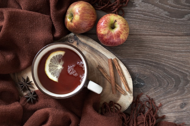 Zdjęcie ceramiczny kubek gorącej herbaty z cytryną, jabłkiem, gwiazdą anyżu, cynamonem na brązowej wełnianej stole. na drewnianym stole. widok z góry