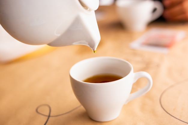 Ceremonia parzenia herbaty soft focus Nalewanie gorącego napoju z białego porcelanowego czajnika do białego kubka jesienią