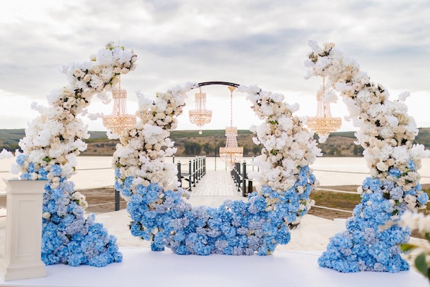 ceremonia ślubna łuk ozdobiony białymi i niebieskimi kwiatami panna młoda i pan młody biorą ślub