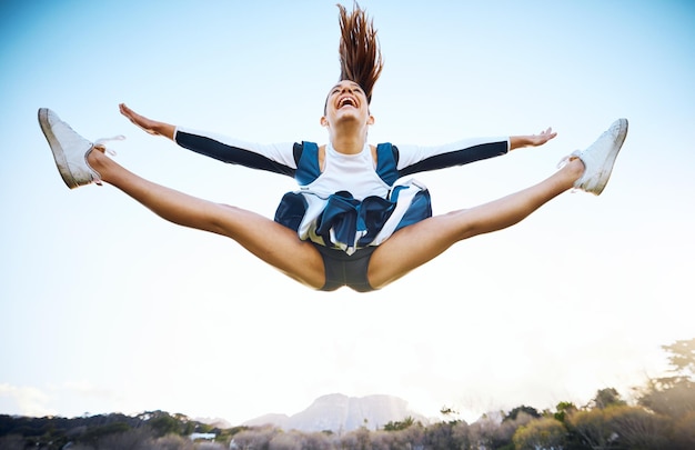 Zdjęcie cheerleaderka niebo i wyniki sportowe z uśmiechem i energią do świętowania na świeżym powietrzu cheerleaderka tańczy lub skacze akrobacje, śmiejąc się z radości podczas treningu wolności lub rywalizacji