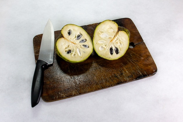 Zdjęcie cherimoya peruwiański egzotyczny owoc pokrojony na dwa plasterki doceniając jego jedzenie i nasiona kładzie się na brązowej drewnianej desce obok kuchennego noża