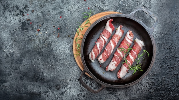 Chevapchichi z rozmarynem w patelni żeliwnej. Kebab Kofta. surowe kiełbaski z mielonej wołowiny lub wieprzowiny z przyprawami zawinięte w boczek. Kiełbaski. baner, menu, przepis na tekst, widok z góry.