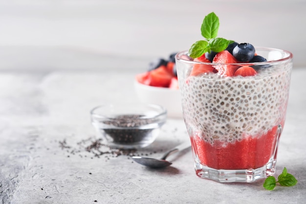 Chia truskawkowy pudding Zdrowe wegańskie śniadanie budyń z nasion chia ze świeżymi jagodami i miętą w szkle na szarym betonowym tle Koncepcja zdrowego odżywiania dieta menu fitness Selektywne skupienie