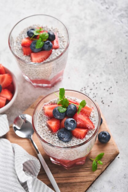 Chia truskawkowy pudding Zdrowe wegańskie śniadanie budyń z nasion chia ze świeżymi jagodami i miętą w szkle na szarym betonowym tle Koncepcja zdrowego odżywiania dieta menu fitness Selektywne skupienie