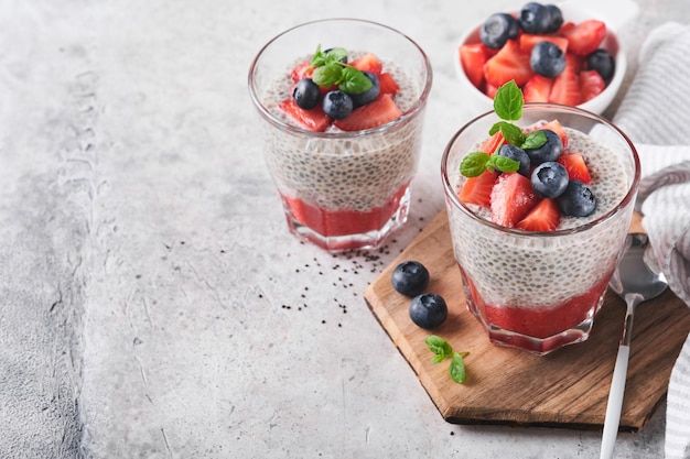 Chia truskawkowy pudding Zdrowe wegańskie śniadanie budyń z nasion chia ze świeżymi jagodami i miętą w szkle na szarym betonowym tle Koncepcja zdrowego odżywiania dieta menu fitness Selektywne skupienie