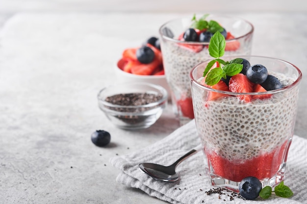 Chia truskawkowy pudding Zdrowe wegańskie śniadanie budyń z nasion chia ze świeżymi jagodami i miętą w szkle na szarym betonowym tle Koncepcja zdrowego odżywiania dieta menu fitness Selektywne skupienie