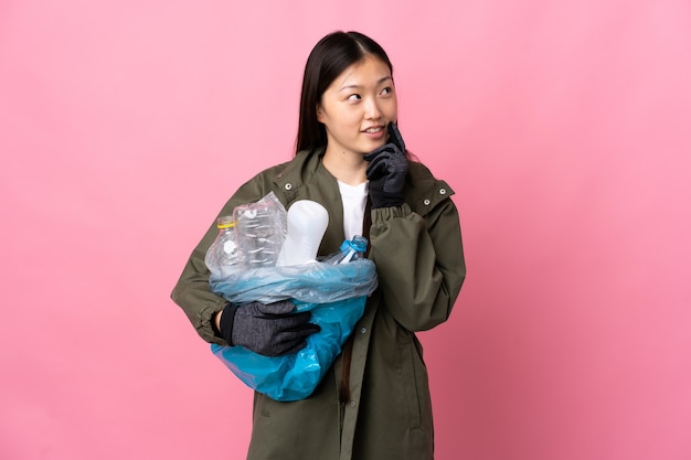 Chinka trzyma torbę pełną plastikowych butelek do recyklingu na białym tle