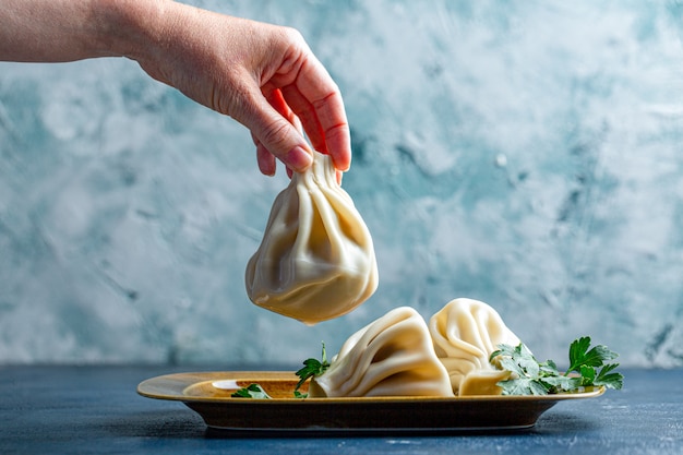 Chinkali, Gruzińskie Pierogi, Tradycyjna Gruzińska Kuchnia. Ręka Cooka Kładzie Chinkali Na Talerzu Z Boku.