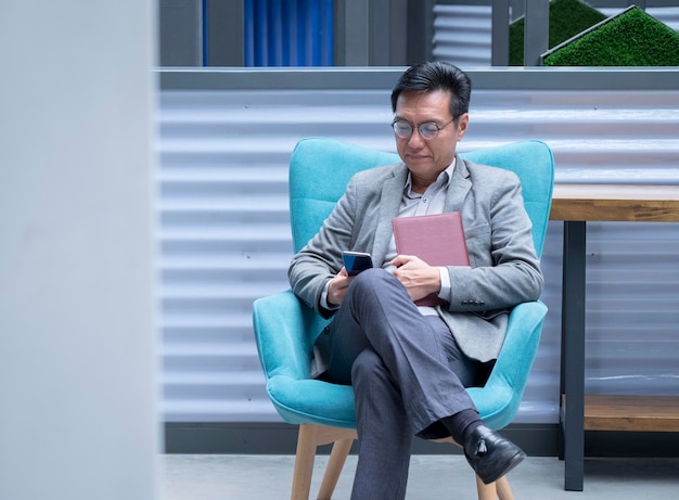 Chiński biznesmen siedzi na krześle i czyta swój telefon komórkowy