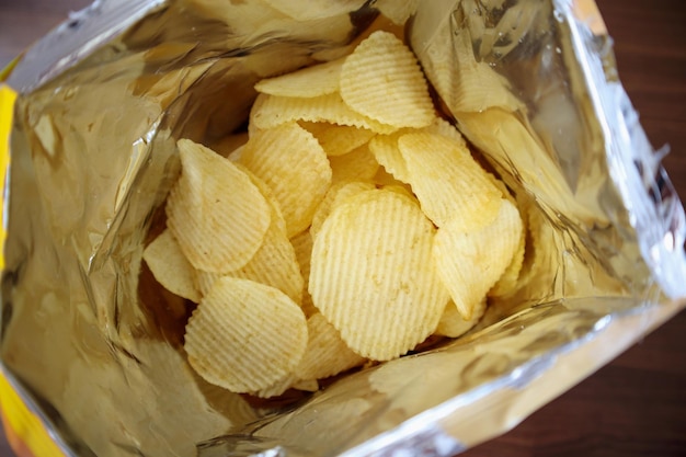 Chipsy ziemniaczane w otwartej torbie na przekąski z bliska na podłodze stołu