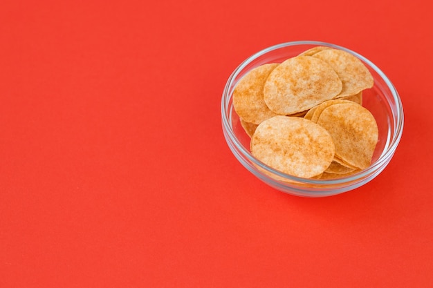 Chipsy ziemniaczane w szklanej misce na czerwonym tle Fast food