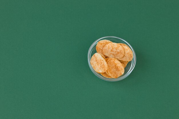 Chipsy ziemniaczane w szklanej misce na zielonym tle Fast food