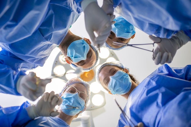 Chirurdzy stojący nad pacjentem przed operacją Wieloetniczny personel medyczny wykonujący operację na pacjencie na sali operacyjnej