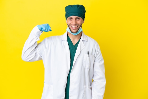 Chirurg blondyn w zielonym mundurze na żółtym tle robi silny gest
