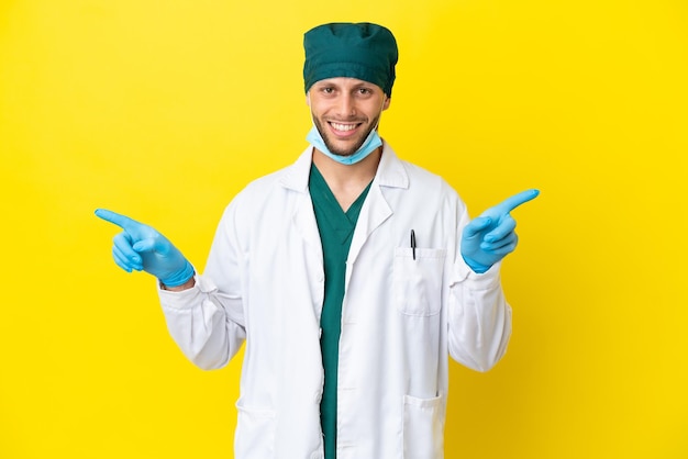Chirurg blondyn w zielonym mundurze na żółtym tle, wskazując palcem na boki i szczęśliwy