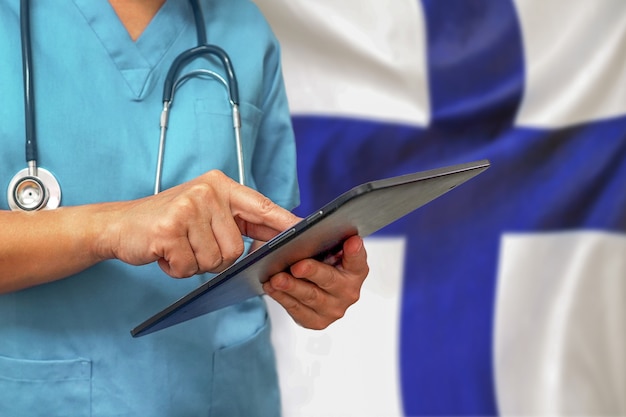 Chirurg lub lekarz za pomocą cyfrowego tabletu na tle flagi Finlandii