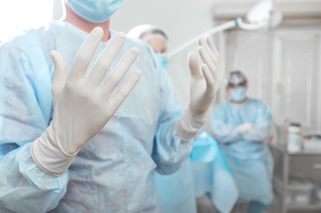 Chirurg podnosi ręce, aby zdezynfekować ręce w białych rękawiczkach przed operacją