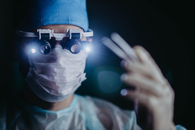 Chirurg W Okularach Z Lupą Okularową Operuje Na Pacjencie W Ciemnej Sali Operacyjnej