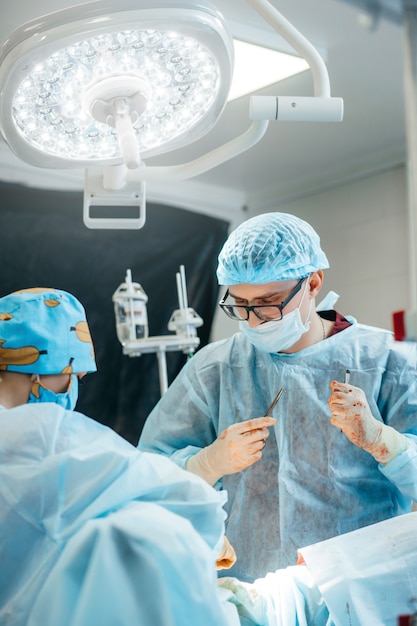Chirurg wykonujący operację piersi w szpitalnej sali operacyjnej. Chirurg w masce noszący lupy chirurgiczne podczas zabiegu.