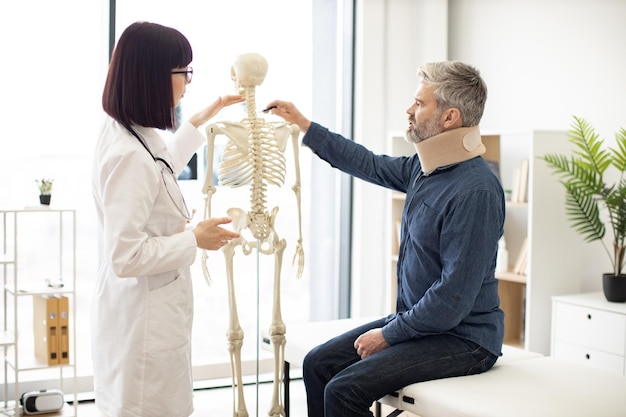Zdjęcie chirurg z dojrzałym mężczyzną oznaczającym kości szyi na modelu w pomieszczeniu
