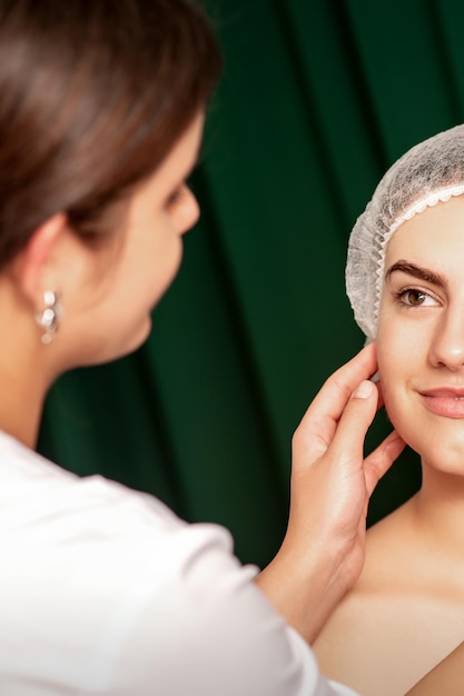 Chirurgia plastyczna i koncepcja urody Profesjonalna kosmetyczka badająca i dotykająca twarzy pięknej młodej uśmiechniętej kobiety rasy kaukaskiej w klinice kosmetologii estetycznej