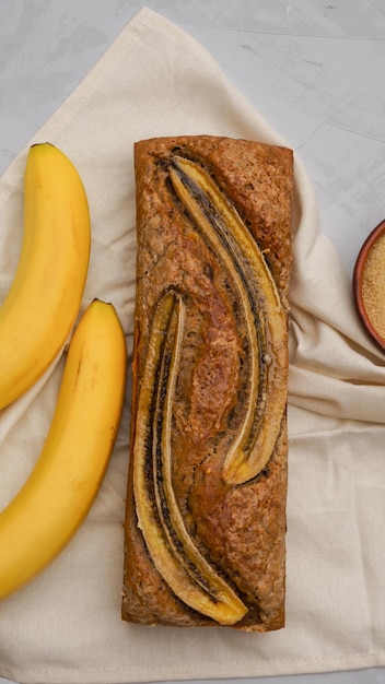 chleb bananowy otoczony świeżymi bananami i składnikami do gotowania leży na zwykłym szarym tle