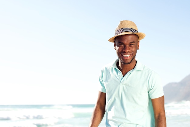 Chłodno młody afrykański mężczyzna z kapeluszem przy plażą