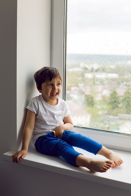 Zdjęcie chłopak w białym podkoszulku i niebieskich spodniach przy oknie