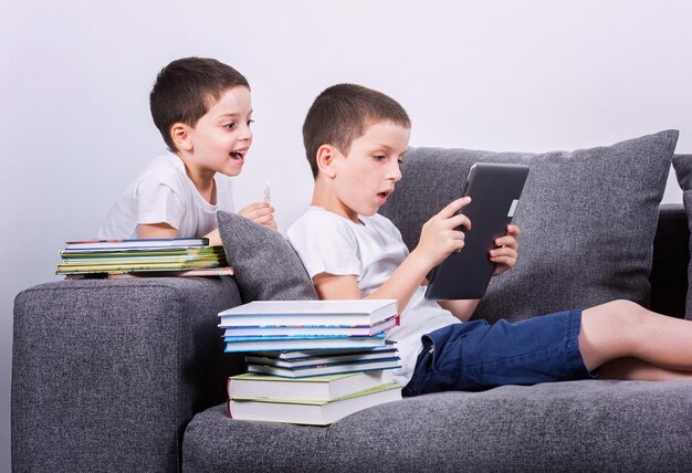 Chłopcy korzystający z tabletu PC na kanapie Portret studyjny Koncepcja cyfrowego świata kontra papierowa książka