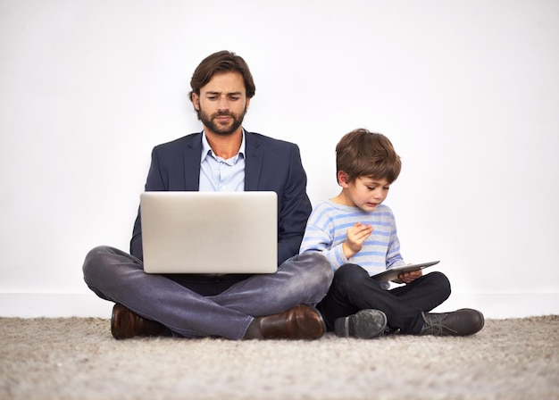 Chłopcy Uwielbiają Swoje Cyfrowe Zabawki Ojciec I Syn Siedzą Na Podłodze Pod ścianą Z Laptopem I Cyfrowym Tabletem