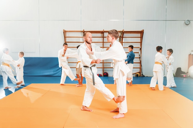 Chłopcy w kimonach ćwiczą sztuki walki na siłowni sportowej. Kid judo, młodzi zawodnicy na treningu w hali.