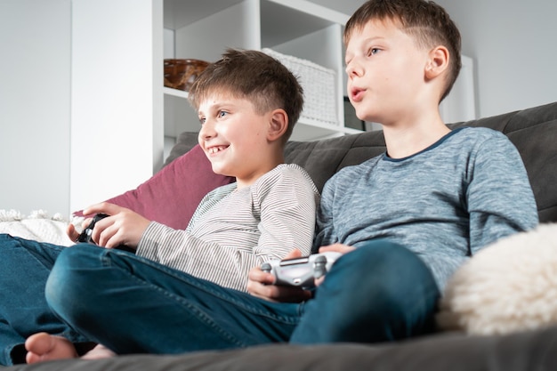 Chłopcy w wieku szkolnym siedzą na kanapie z joystickami do gier od dołu Widok Dzieci grają w gry wideo Styl życia najlepszych przyjaciół