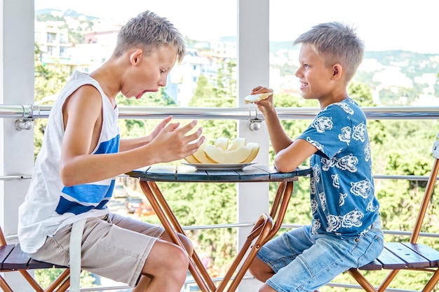 Chłopcy ze szkoły z podekscytowaniem lubią jeść świeżego melona na hotelowym tarasie