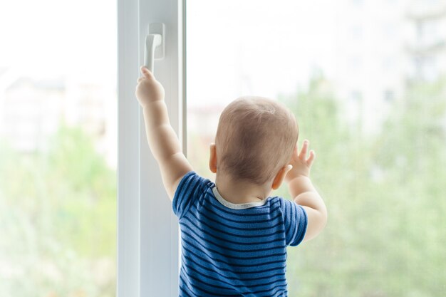 Chłopczyk siedzi na parapecie i próbuje otworzyć okno pociągając za klamkę