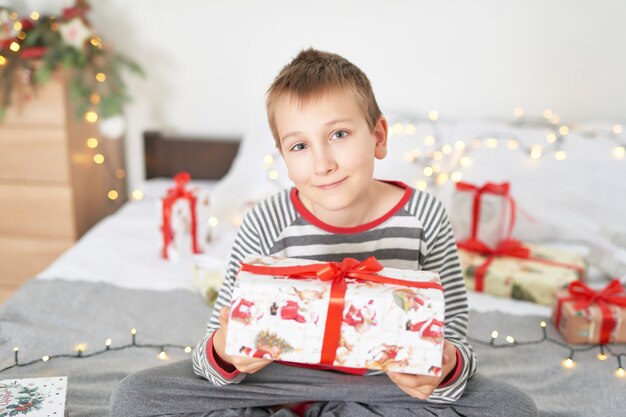 Zdjęcie chłopczyk z prezentami świątecznymi w domu na łóżku z wystrojem świątecznym
