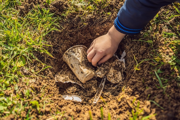 Chłopiec bawi się w recykling, po kilku zakopuje plastikowe naczynia jednorazowe i naczynia biodegradowalne